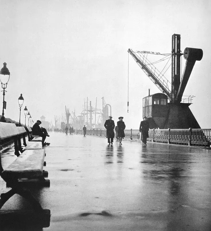 Wandelaars op het natte Wandelterras langs de Scheldekaaien met op de achtergrond een havenkraan in Antwerpen (1946) door Cas Oorthuys